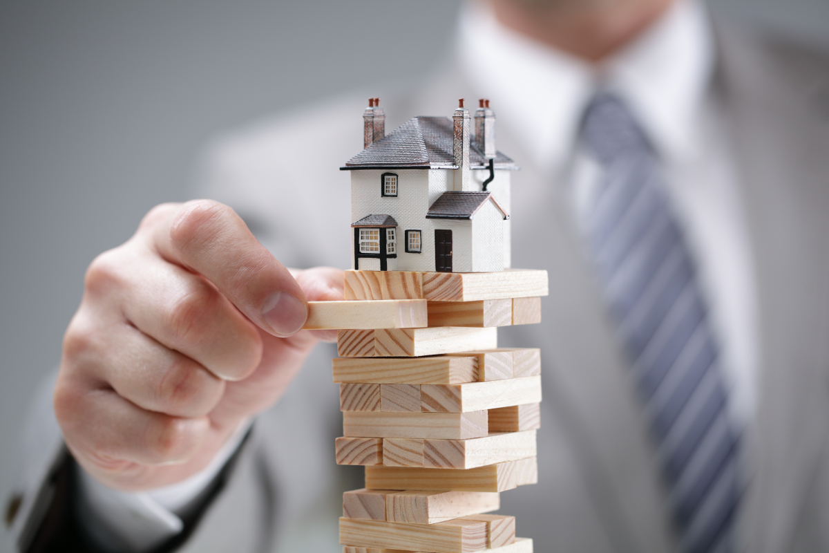 Courtier Immobilier à Toulouse – Paires de mains de deux personnes tenant un stylo et une calculatrice au-dessus d’un document et d’une maison miniature.