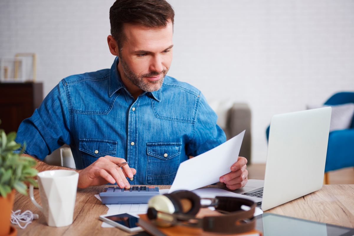 Un homme en train de calculer ses dépenses et recettes à l’aide d’un ordinateur et d’une calculatrice