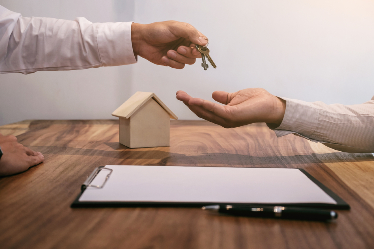 Changement de propriétaire locataire — un échange de clés au-dessus d’un contrat de bail posé à côté d’une maison miniature sur un bureau