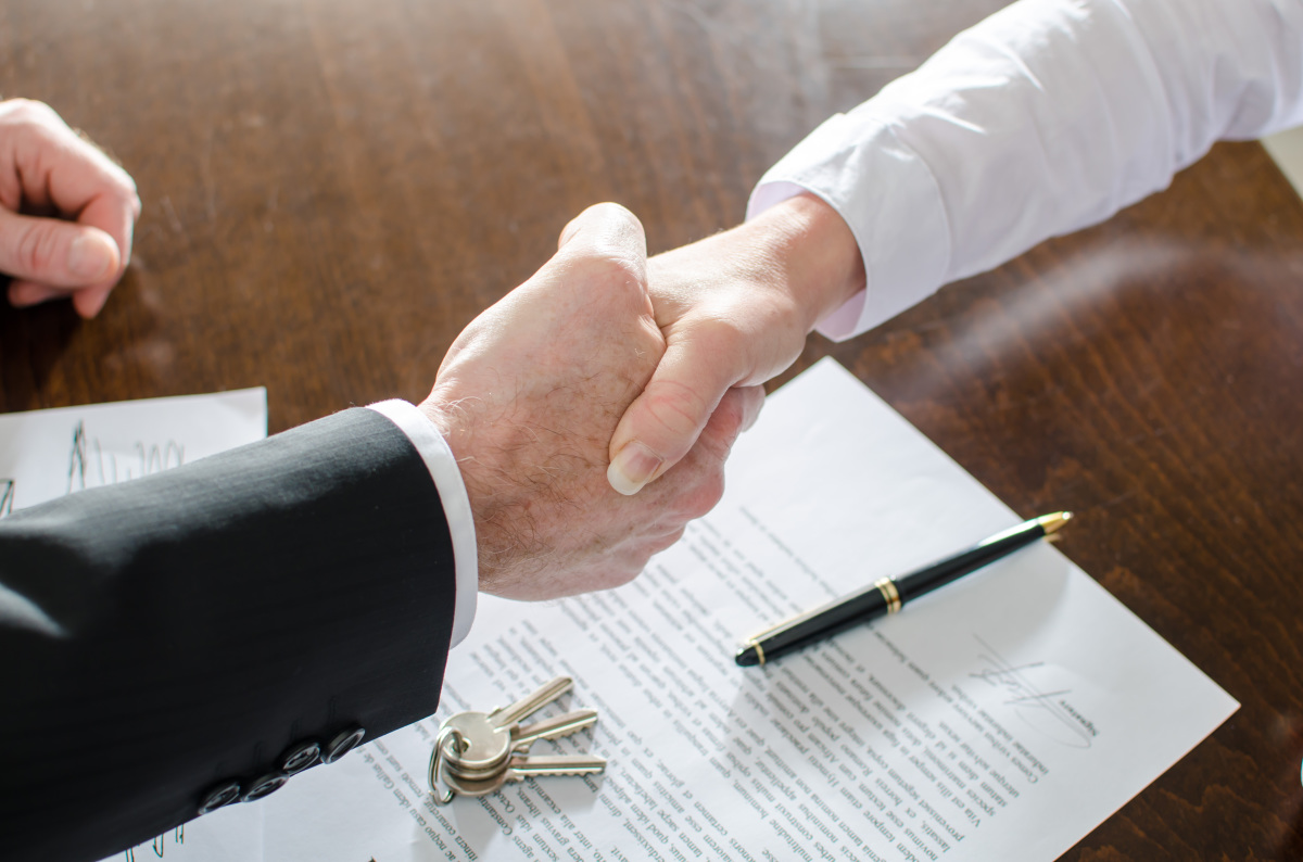 Travaux Modificatifs Acquéreurs – Deux personnes se serrent la main au-dessus d’un contrat signé et d’un trousseau de clés