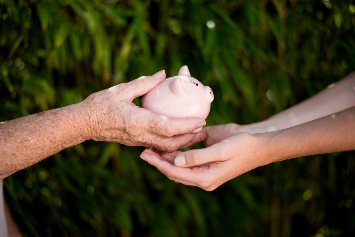 Les mains d’une personne âgée tendent une tirelire à une personne plus jeune