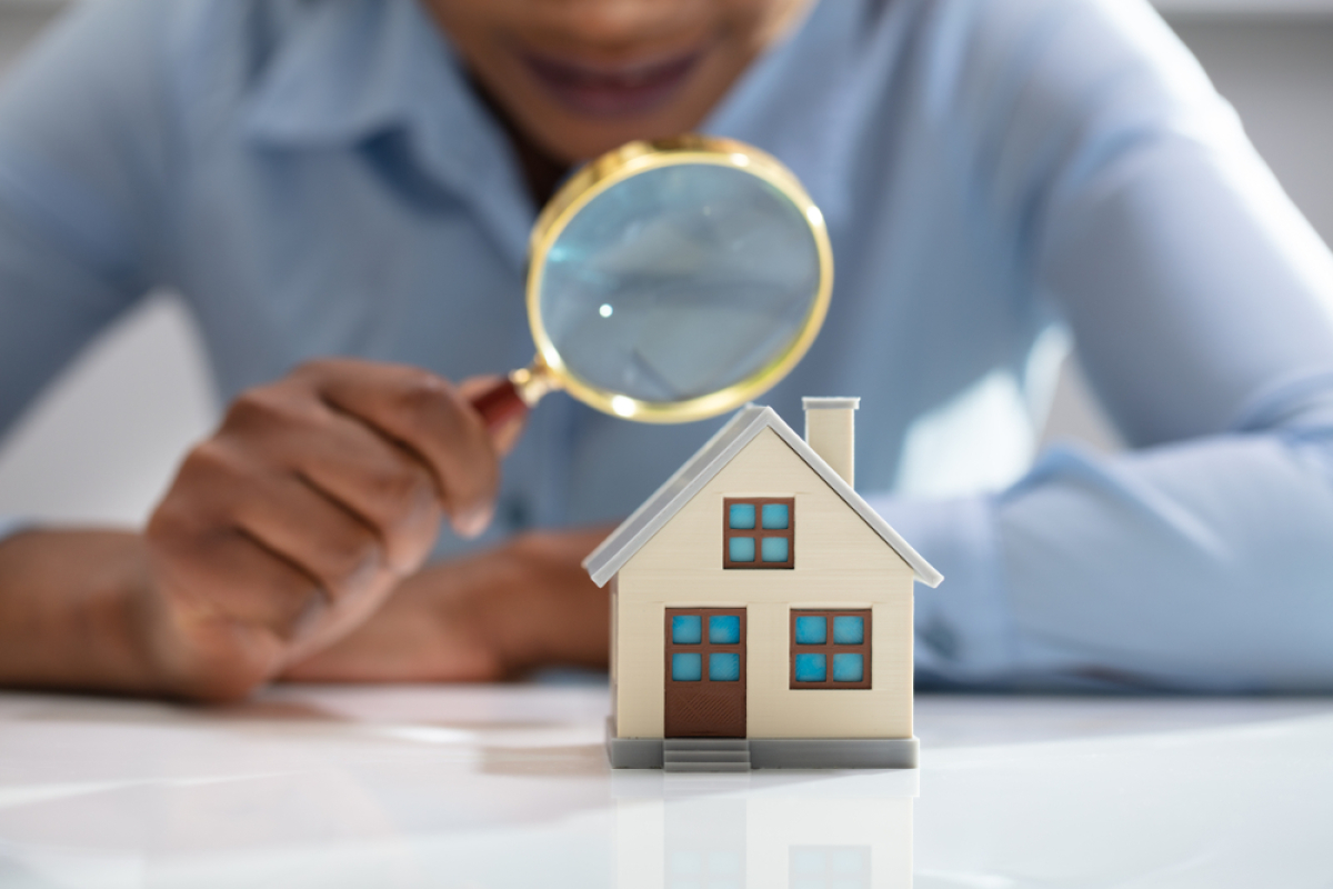 Pinel+ - Un homme regardant à travers une loupe une maquette de maison