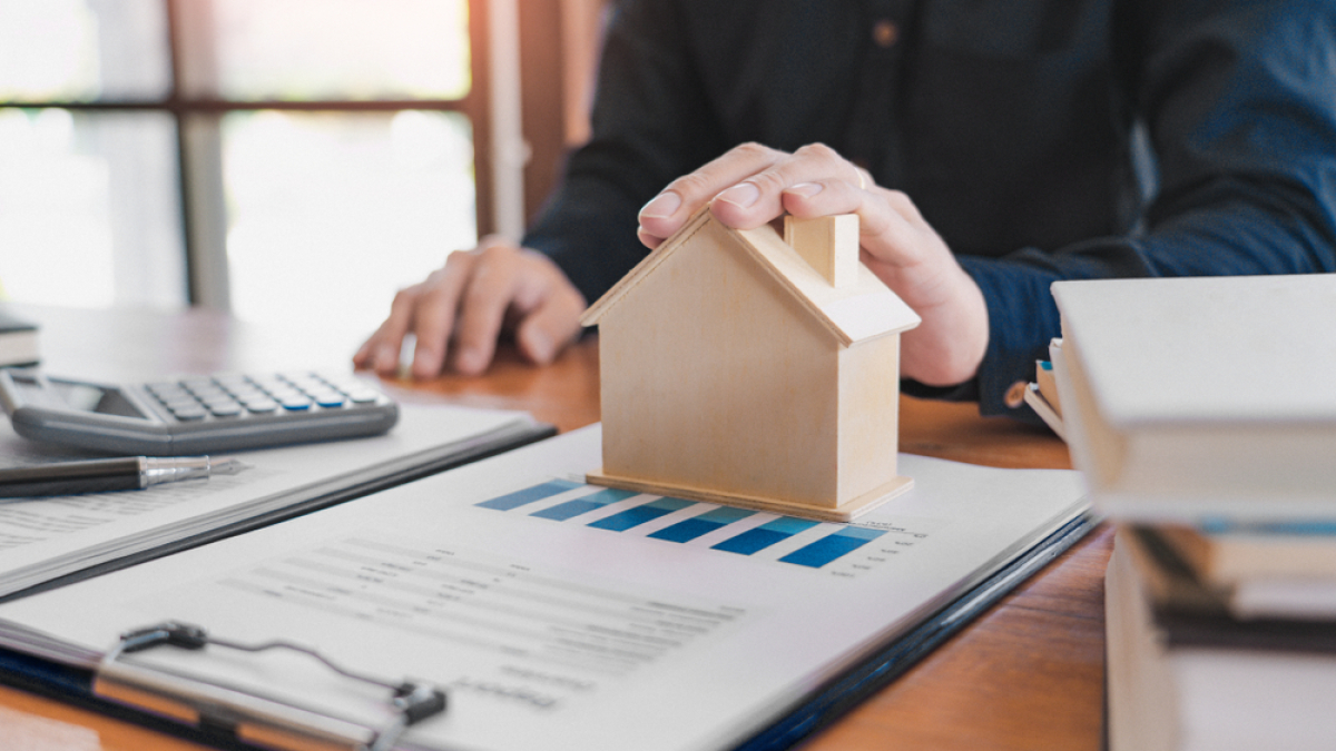 Investissement LMNP Toulouse — une personne faisant des calculs pose sa main sur une maison miniature en bois