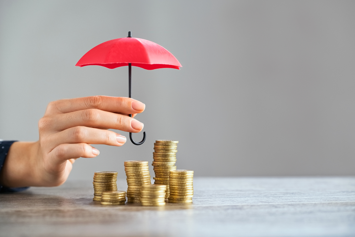Garantie Loyers Impayés – une main place un parapluie miniature au-dessus de tas de piècettes