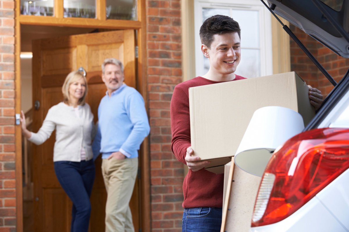 Pinel location famille — Un fils adulte quitte met un carton dans sa voiture tandis que ses parents adultes regardent depuis le pas de porte