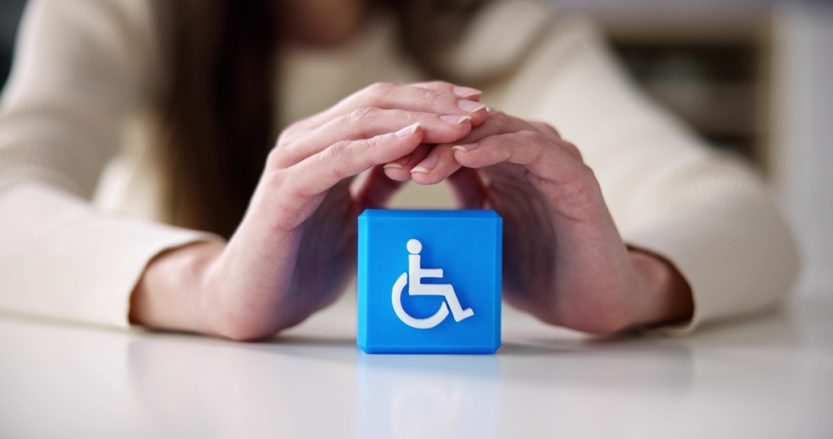 Normes PMR logement neuf – Une personne qui protège avec ses mains un cube avec le logo du handicap