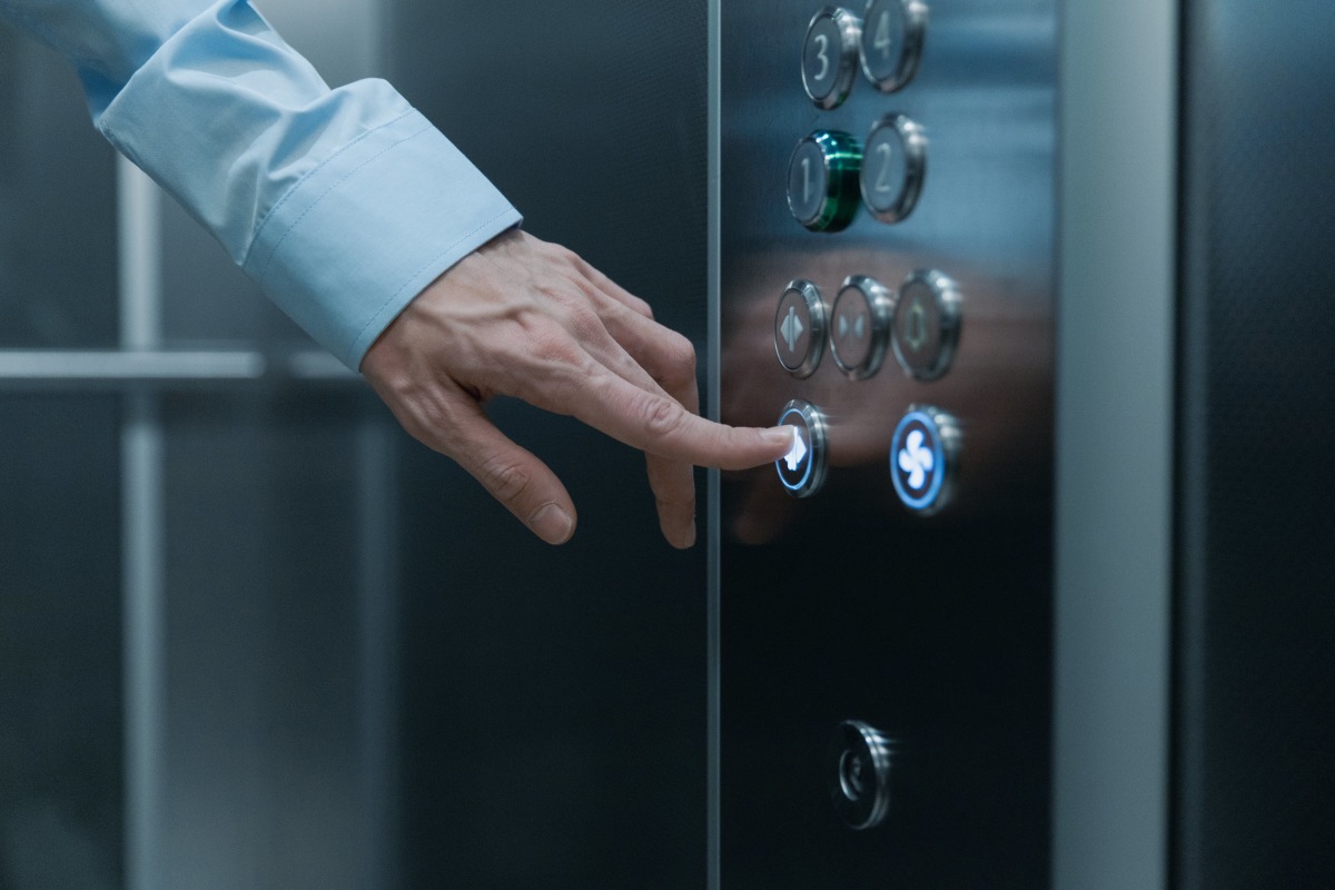 Comment réduire les charges de copropriété – Une personne appuie sur un bouton d’ascenseur