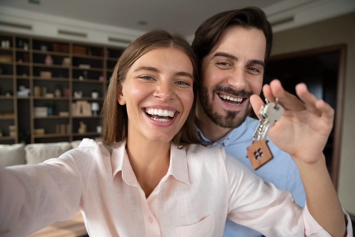 Retour de lot immobilier neuf — Un jeune couple souriant tenant les clés d’un appartement neuf
