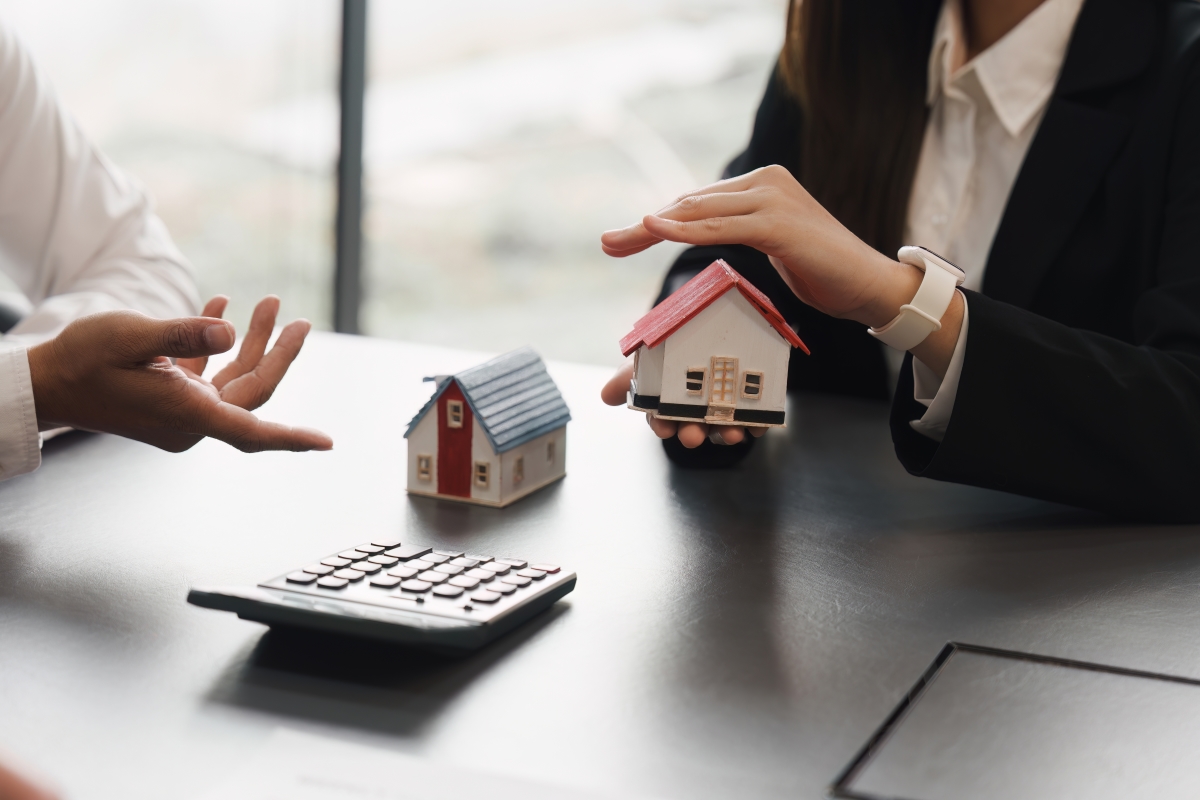 Accompagnement immobilier — des mains durant une négociation autour de petites maquettes de maisons