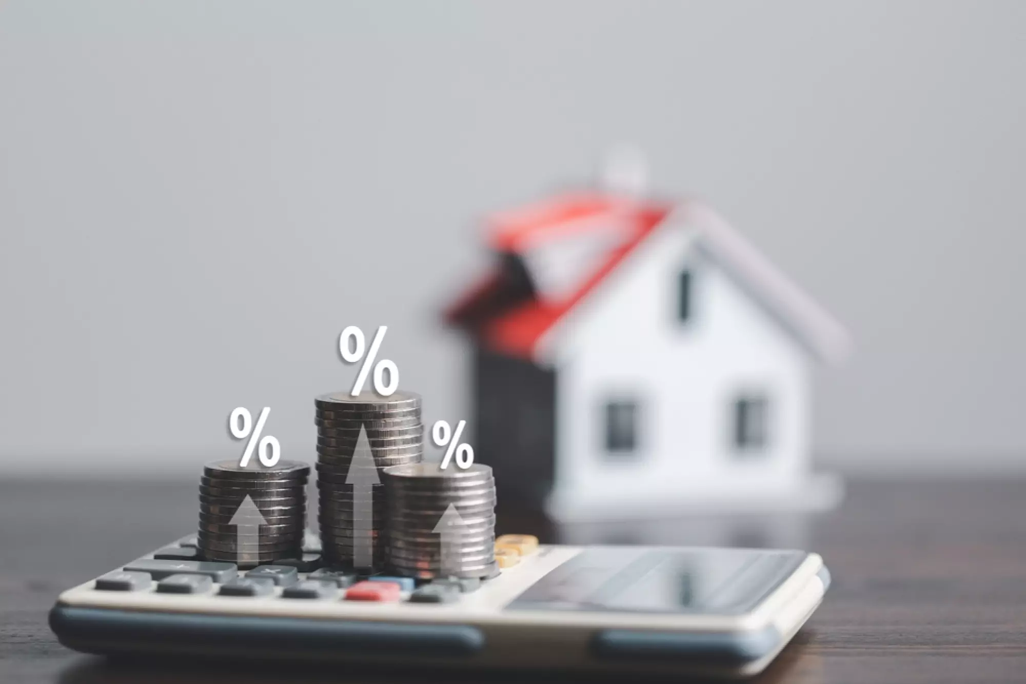 Des piles de pièces avec pourcentages sur une calculatrice avec une maison en fond